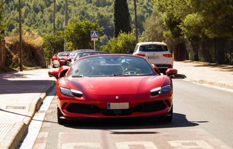 Ferrari 296 GTB rojo circulando por una calle de ruta hacia el Restaurante Arrels.